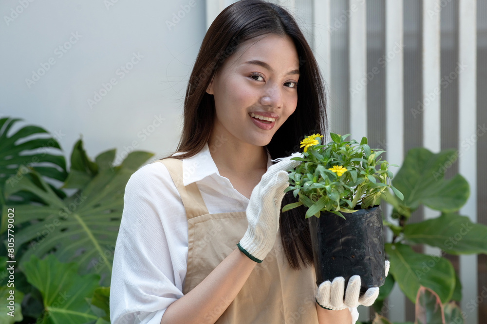 Beautiful young woman spends her weekends tending to the plants in her garden, carrying a plant bag, preparing to transplant it into a pot, looking at camera