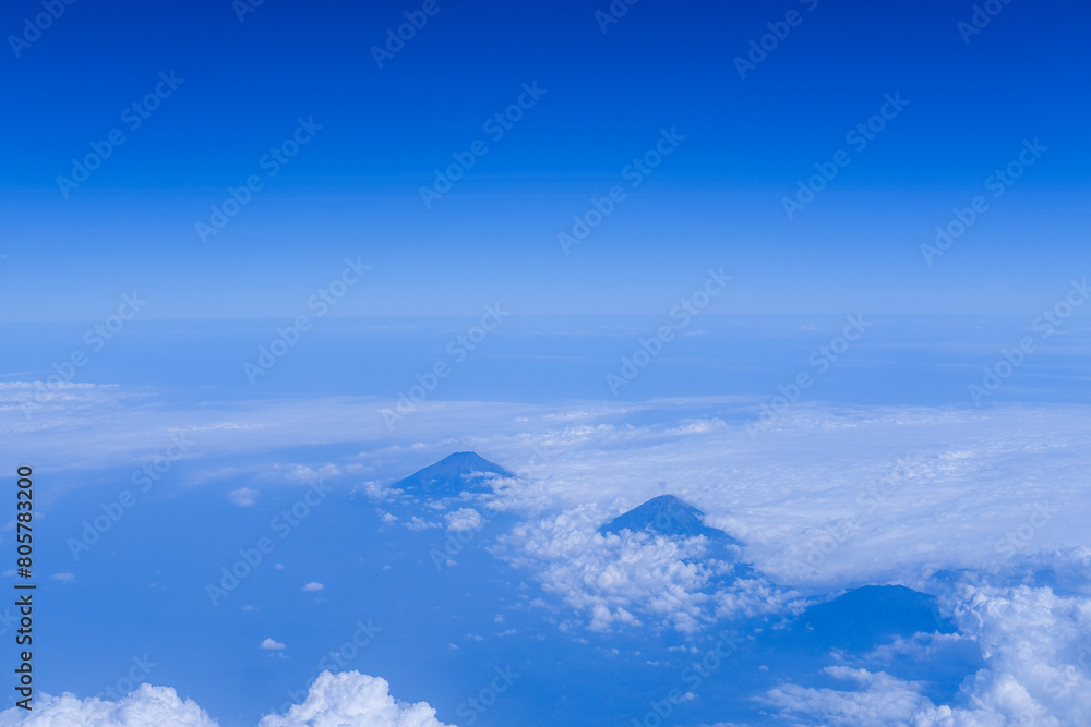 Aerial view from a plane over Java Island, showcasing majestic mountains rising through a sea of clouds under a clear blue sky Aerial view from a plane over Java Island, showcasing majestic mountains rising through a sea of clouds under a clear blue sky