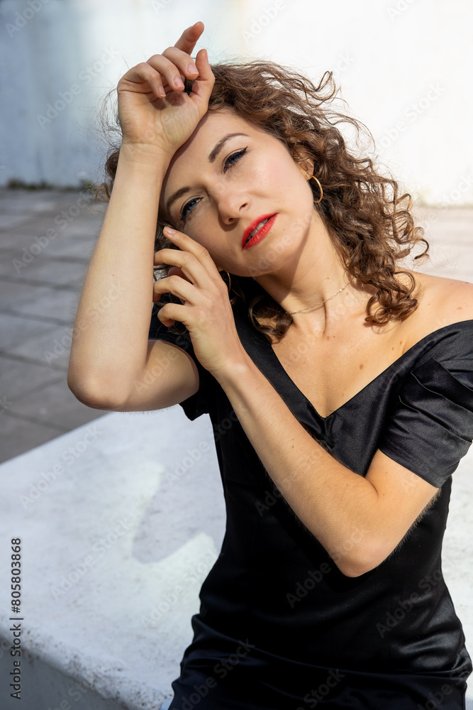 Serene curly woman sitting on bench and looking at camera. Serene curly woman sitting on bench and looking at camera.