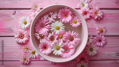   A pink table is adorned with a bowl of pink and white daisies Nearby  a bouquet of matching flowers adds to the scene