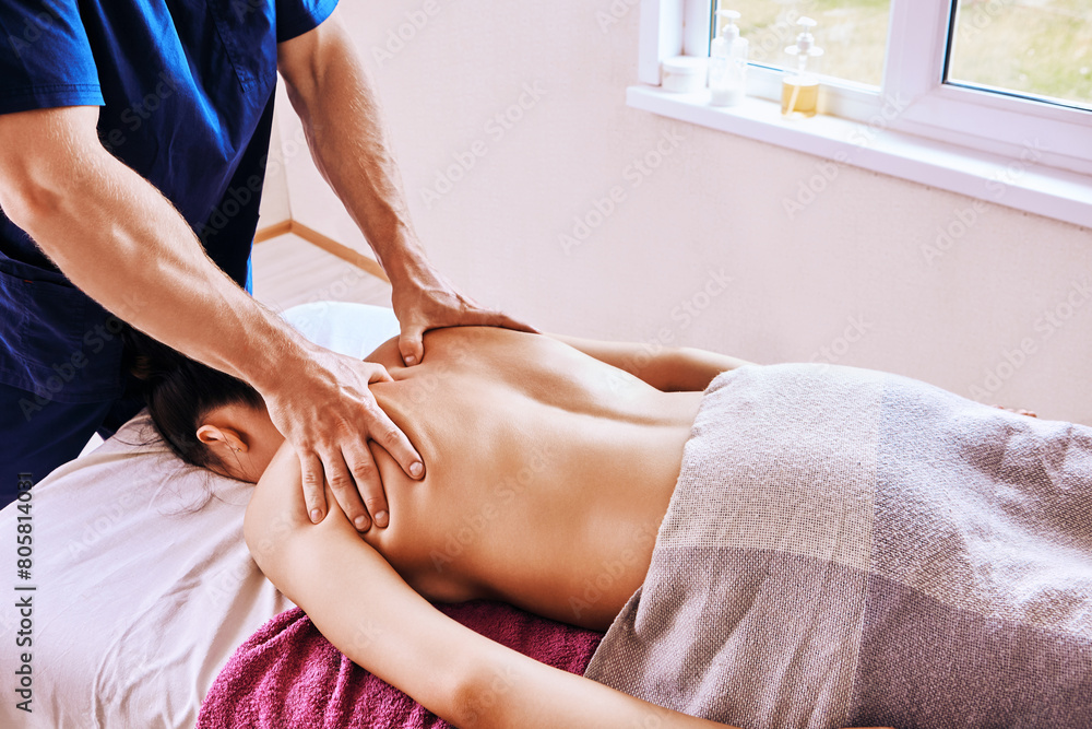 Woman lies face down on massage table, masseur massages her shoulder area, pressing with his fingertips, deep stroking and pressure tissue massage. Woman lies face down on massage table, masseur massages her shoulder area, pressing with his fingertips, deep stroking and pressure tissue massage.