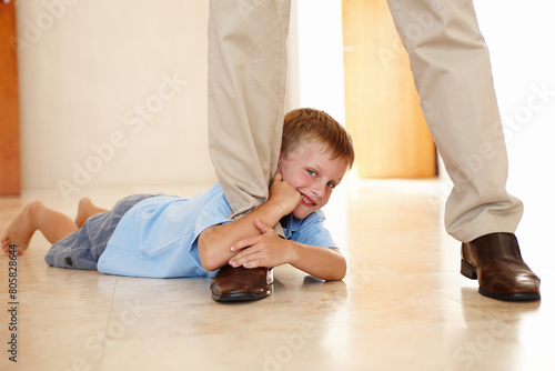 Φωτογραφία Leg, child and holding on parent in portrait, play and hanging on father for game on floor in home