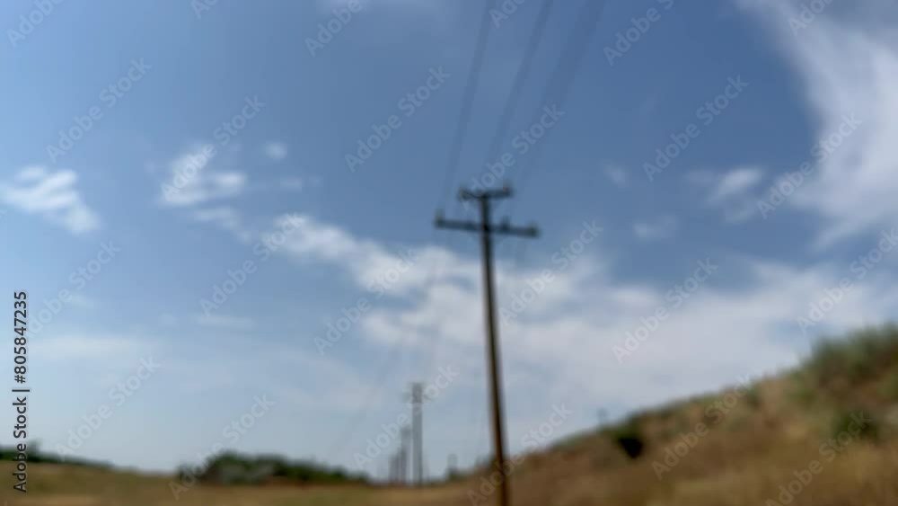 Concrete pillars with wires torn from explosions stand along railway with an iron bridge laid across dirt road. War in Ukraine