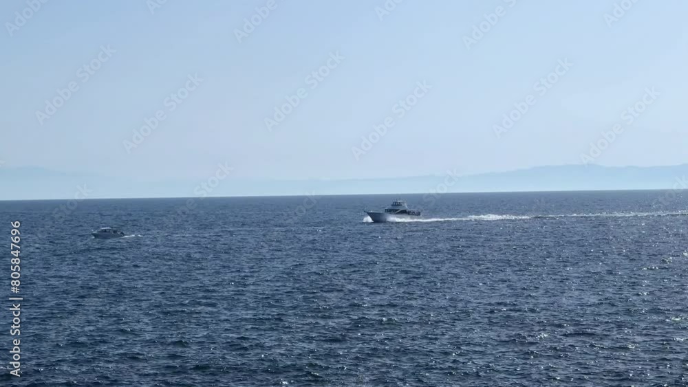 Boat speeding over the open sea with distant mountainous coastline on a clear day Boat speeding over the open sea with distant mountainous coastline on a clear day
