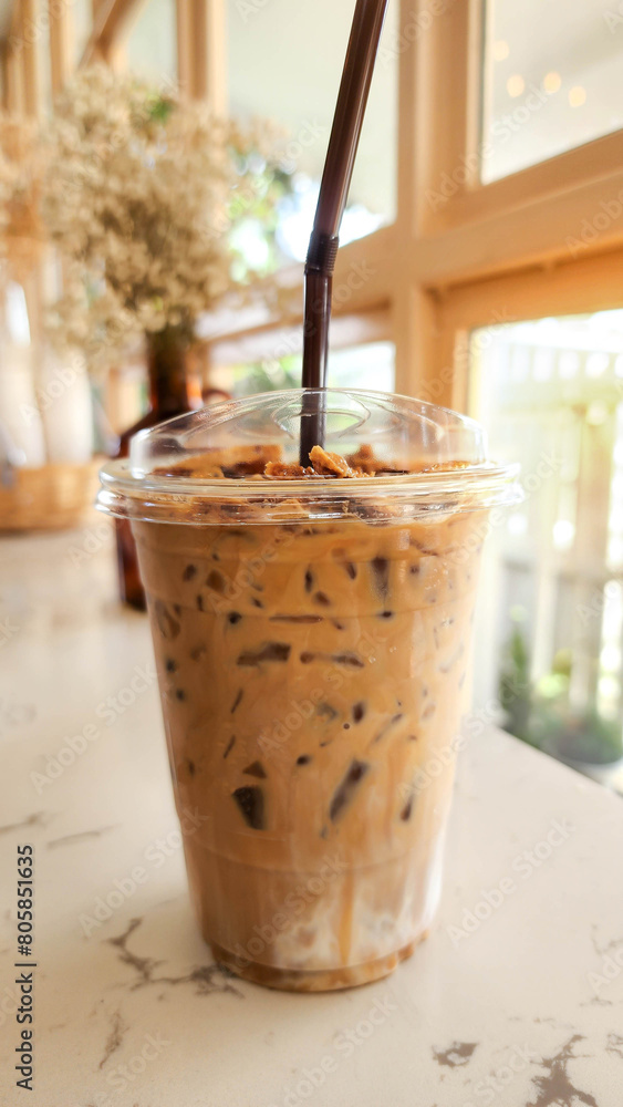 Iced cappuccino coffee in a clear take-home cup. There are dried flowers in the background. Iced cappuccino coffee in a clear take-home cup. There are dried flowers in the background.