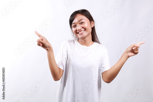 Portrait of young beautiful asian woman pointing fingers left and right, making decision, showing two variants choices, standing over white background