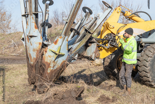 Male worker operates tree transplanter heavy machine. Landscaping, seasonal agricultural engineering, large trees landing machines.