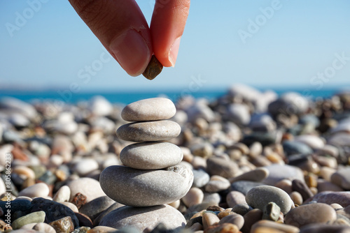 Balance of mind - abstract - hand putting pebble on the tower of stones on the sunny beach photo