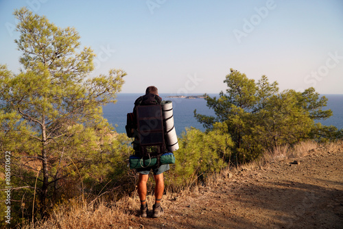 A man in shorts with a backpack, tourist mat, tent and a solar panel on it looks at the islands in the Mediterranean Sea on the Lycian Way