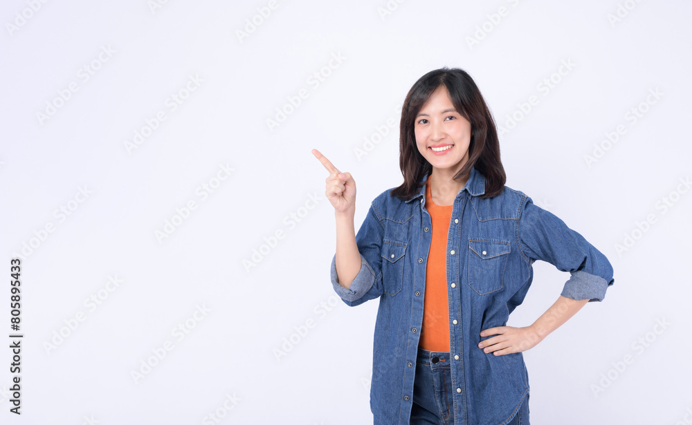 A Young asian woman wearing orange t shirt and denim jean while pointing finger to free copy space isolated on white studio background A Young asian woman wearing orange t shirt and denim jean while pointing finger to free copy space isolated on white studio background