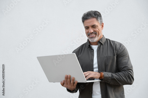 Mature 40s Indian happy man using wireless pc for business solutions, isolated on white background. Middle age freelance entrepreneur, latin hispanic businessman holding laptop computer, working busy