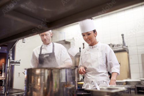 Chef  teamwork and cooking in professional kitchen at stove top or fine dining cuisine  hospitality or service. Man  woman an hat as restaurant career or food preparation or dinner rush  meal or help