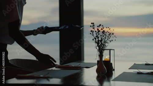 Close up of silhouette of a waiter serving a table in a restaurant, window on background. Concept of evening romantic diner on sunset, premium service