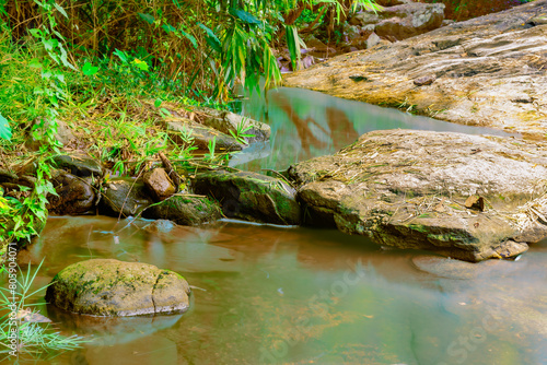 Small stream with gentle smoothing flowing water moves through mossy rocks in the natural water source