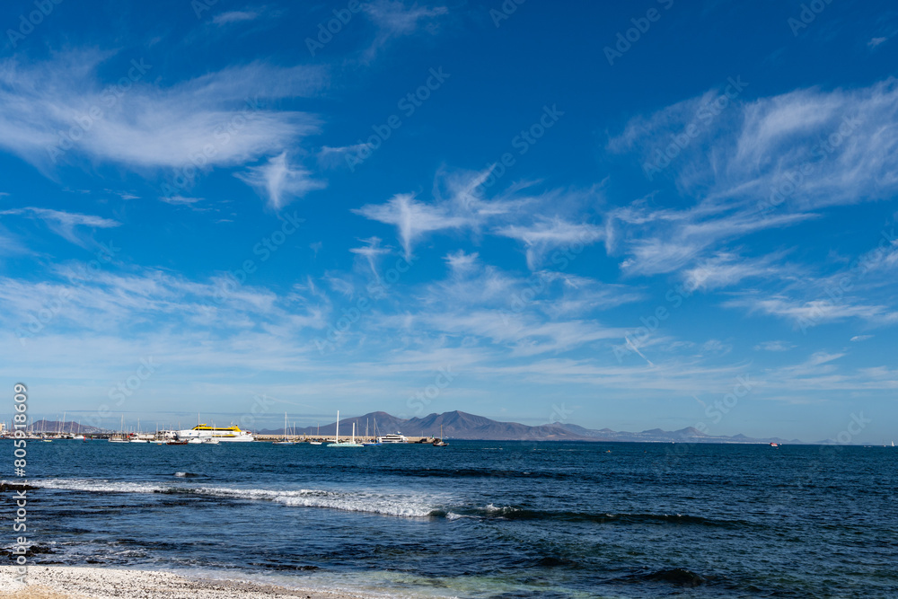 Walking on sea promenade in Corralejo along black rocks, blue water, view on Lanzarote island, Fuerteventura, Canary islands, Spain Walking on sea promenade in Corralejo along black rocks, blue water, view on Lanzarote island, Fuerteventura, Canary islands, Spain