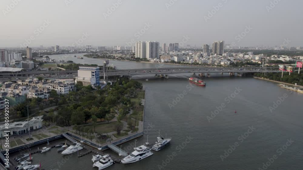 Ho Chi Minh, Saigon, Vietnam, with the river, a bridge, and a cargo vessel passing under it, aerial drone video during sunset Ho Chi Minh, Saigon, Vietnam, with the river, a bridge, and a cargo vessel passing under it, aerial drone video during sunset