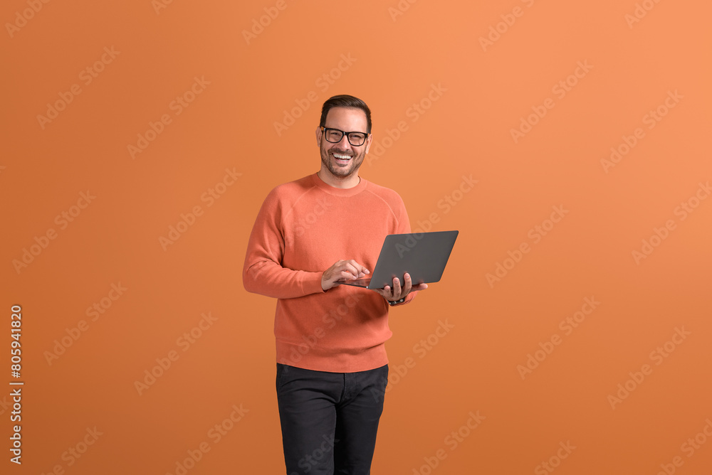 Portrait of happy confident businessman checking e-mails over wireless computer on orange background Portrait of happy confident businessman checking e-mails over wireless computer on orange background