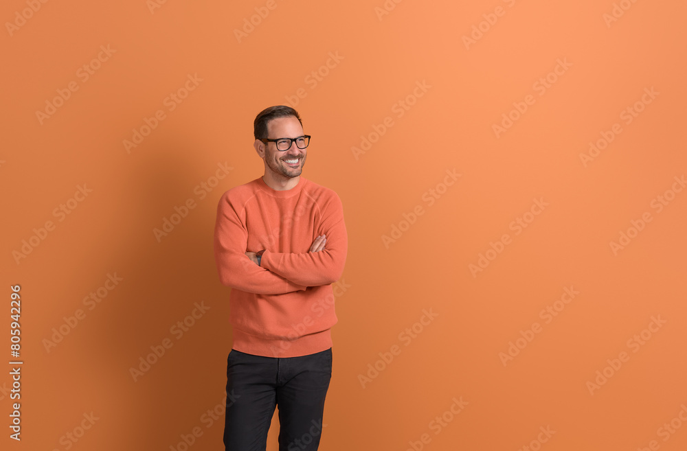Smiling young businessman with arms crossed looking away and thinking on isolated orange background Smiling young businessman with arms crossed looking away and thinking on isolated orange background
