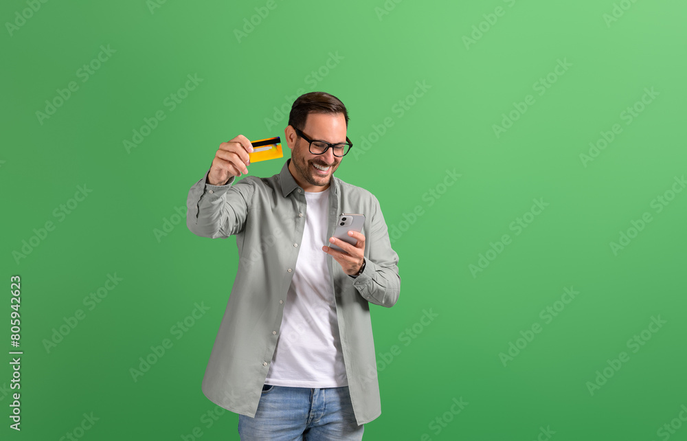 Happy handsome entrepreneur texting over smart phone and showing credit card on green background Happy handsome entrepreneur texting over smart phone and showing credit card on green background