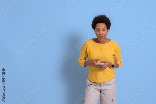 Portrait of shocked young businesswoman with mouth open using mobile phone over blue background