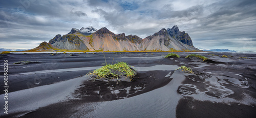 Landscape in panorama format of the famous mountain range Vestrahorn with a beach of black volcanic sand and low grass covered dunes in the foreground, Iceland 