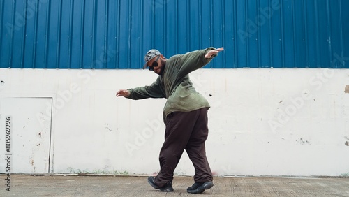 Hipster dancing b-boy foot step at street with blue wall. Asian break dancer practice street dance while stretch arms. Hip hop choreographer perform energetic dance. Outdoor sport 2024. Endeavor.