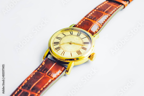 A classic wristwatch with a brown leather strap and a gold face with Roman numerals, displaying the current time, resting on a pristine white background.