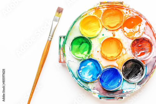 A colorful watercolor palette with a few wells filled with paint and a paintbrush resting on the edge, on a pristine white background.