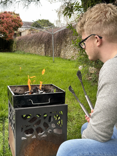 Vertical cropped rear view shot of a man starting fire in a grill pit