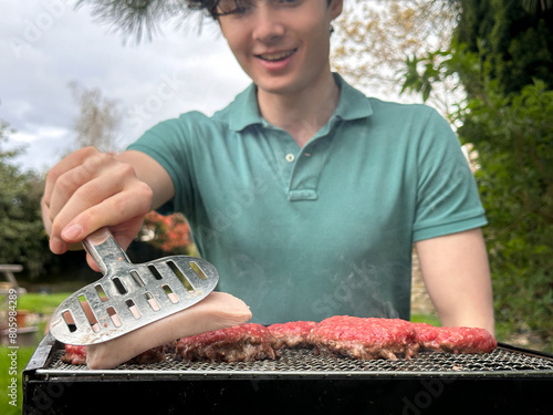 Selective focus on hot dogs on a grill, young man enjoying garden bbq party