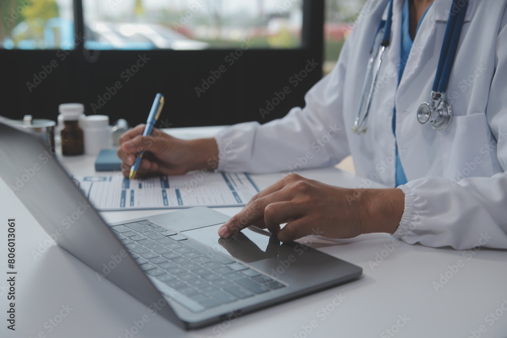 A professional and focused Asian female doctor in scrubs is working and reading medical research on her laptop in her office at a hospital. A professional and focused Asian female doctor in scrubs is working and reading medical research on her laptop in her office at a hospital.