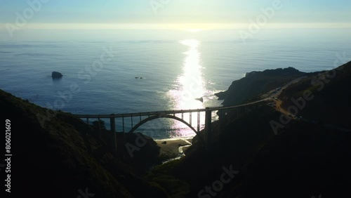 4k cinematic aerial scenic sunset. Panoramic aerial view over arch Bixby Creek Bridge against the backdrop of the blue Pacific Ocean. The sun sinks into the waves on the horizon. Nature of Big Sur. 
