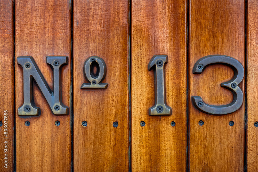 Close-up of a weathered No 13 sign affixed to the wooden planked exterior of a train wagon, stirring feelings of superstition surrounding the infamous number thirteen, associated with misfortune. Close-up of a weathered No 13 sign affixed to the wooden planked exterior of a train wagon, stirring feelings of superstition surrounding the infamous number thirteen, associated with misfortune.