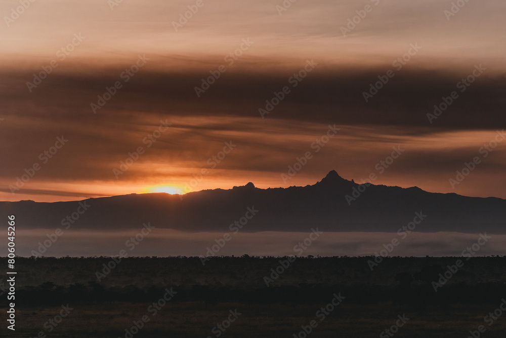 Obraz premium Fiery sunset silhouettes Mount Kenya over misty landscape