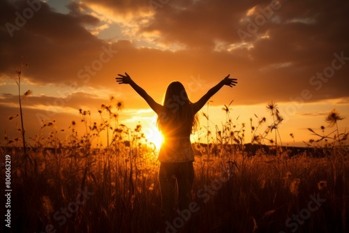 Young woman standing with arms outstretched in a field of wheat during sunset