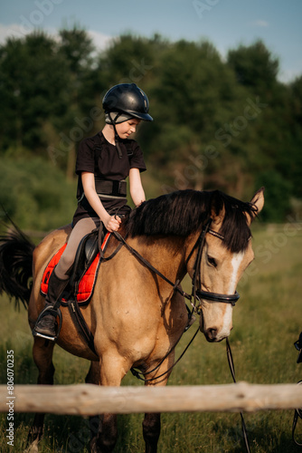 A teenage boy in a helmet learns horse riding in the summer, the instructor teaches the child equestrianism.