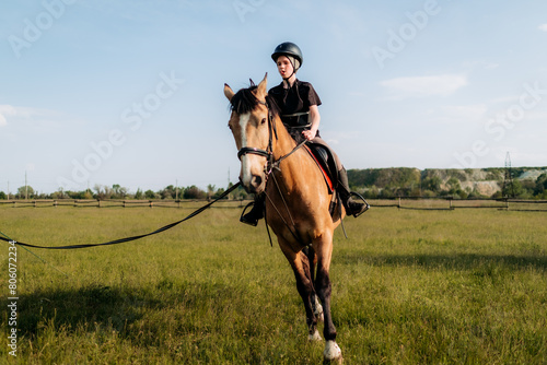 A teenage boy in a helmet learns horse riding in the summer, the instructor teaches the child equestrianism. © sushytska