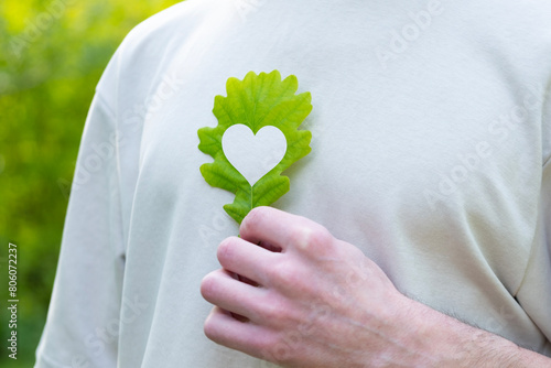 Fotografie young man holds green heart-shaped leaf close to heart, happiness and health, ov