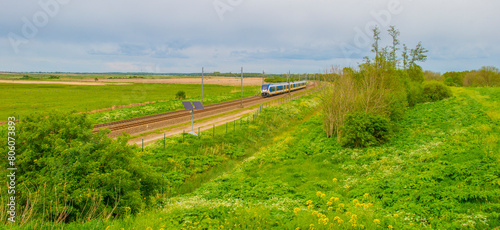 Train riding on a railroad track in wetland below a blue cloudy sky in springtime, Almere, Flevoland, The Netherlands, May 4, 2024