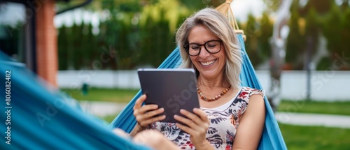Happy woman reading on tablet while relaxing in a hammock outdoors.