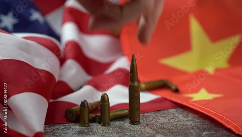 Hand of unrecognizable person placing a large caliber bullet in the middle of an American and Chinese flag. 