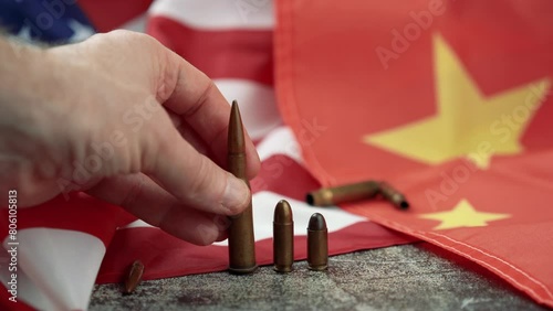 Hand of unrecognizable person leaving several bullets of different caliber in the middle of an American and Chinese flag. 