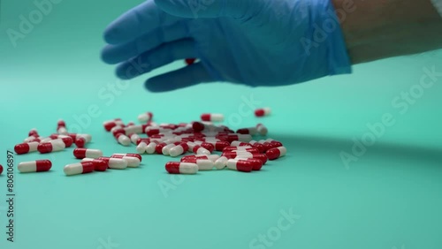 Hand with doctor's glove throwing a pile of capsules on a green table. 
