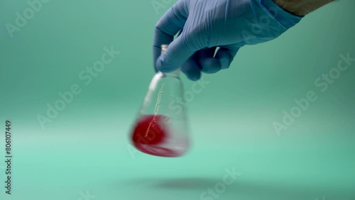 Hand of anonymous doctor in latex glove holding conical flask with red chemical sample in laboratory during diagnostic test