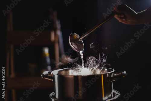 A boiling pot steams up as a chef uses a ladle to stir soup in a cooking pot in a restaurant.