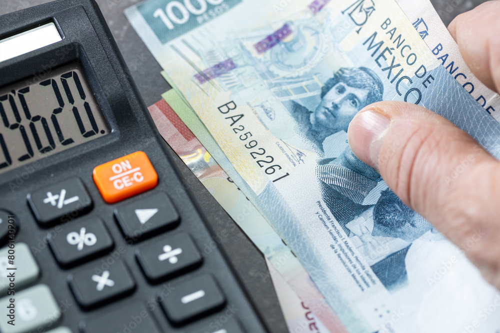 Mexican pesos banknotes, Calculator and money file, financial settlements, household budget, taxes, Mexico currency exchange rate, financial analysis, economic and business concept Mexican pesos banknotes, Calculator and money file, financial settlements, household budget, taxes, Mexico currency exchange rate, financial analysis, economic and business concept