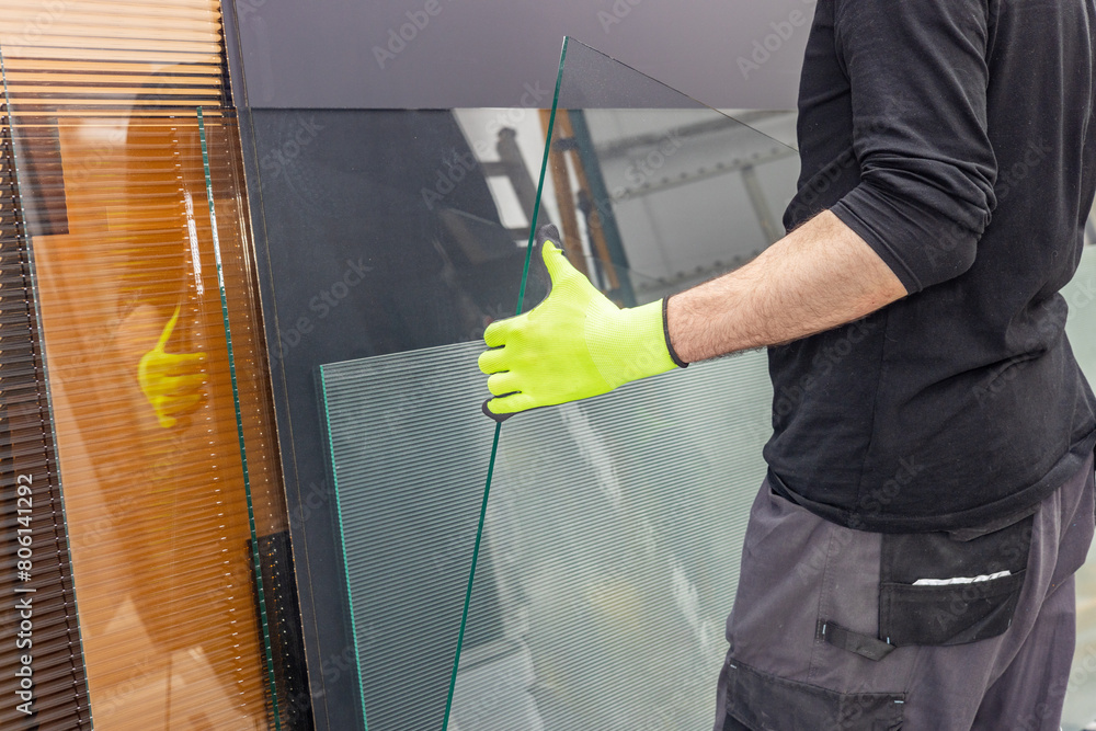 A glazier lifts a glass pane from a rack of glass in a factory