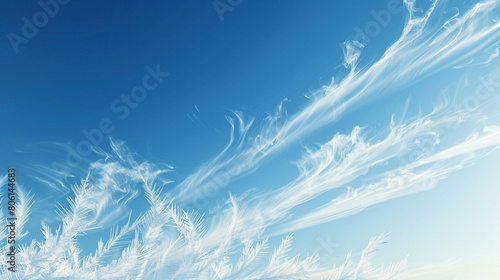 Wispy trails of smoke in frosty blue and white, mimicking the chilly air of winter mornings, set against a clear sky-blue background. © Susan