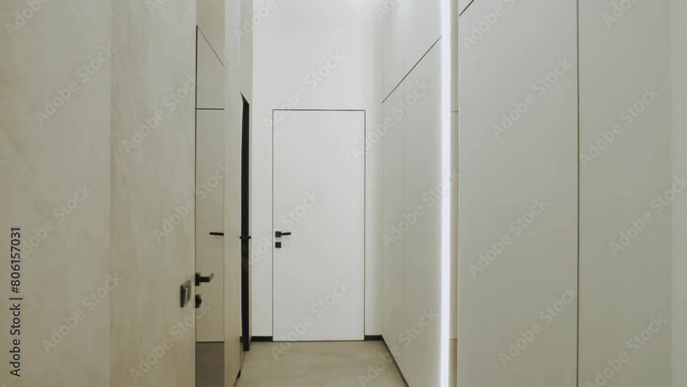 A hallway in a building with white walls, a wooden door, and a handle A hallway in a building with white walls, a wooden door, and a handle