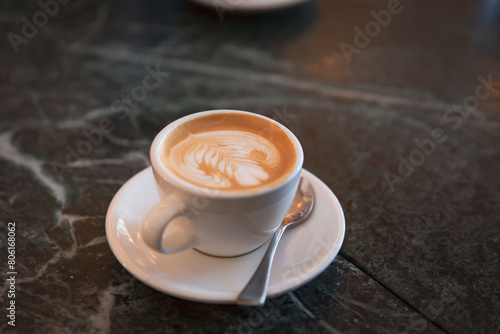 Elegant Cappuccino with Leaf Pattern Latte Art in White Ceramic Cup, Set on a Marble Cafe Table